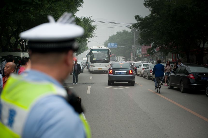 A traffic police gestures to the bus, designated to tranfer test takers of this year&apos;s national college entrance examination to approach the school where the exams are held shortly before the final test ends on Saturday afternoon, June 8, 2013. A total of 72, 736 students in Beijing have registered to sit this &apos;big test.&apos; [Photo / Chen Boyuan]