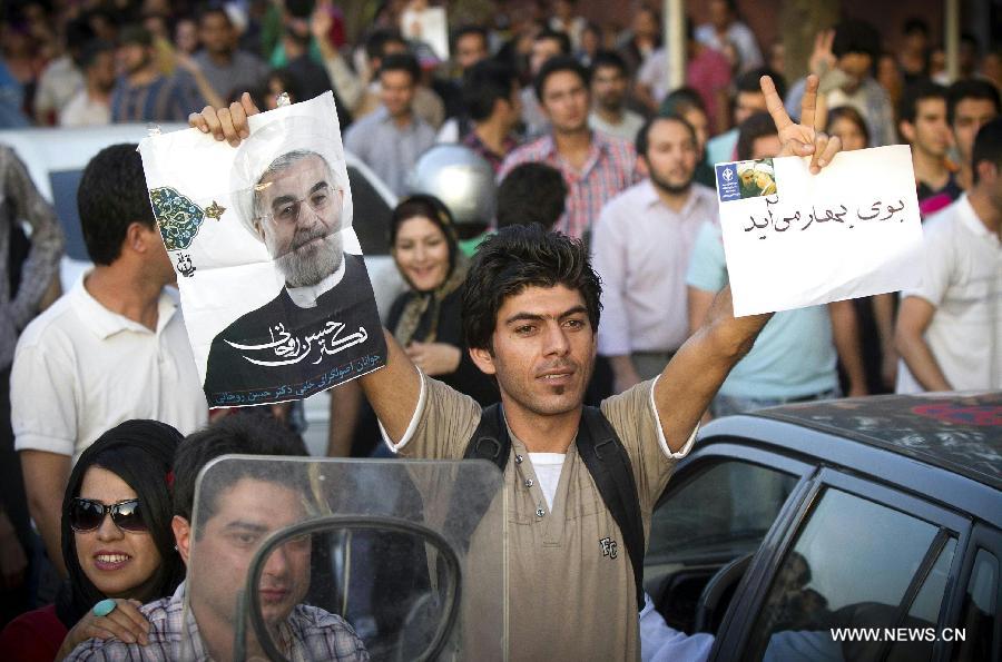 A man raises a poster of Iran's former nuclear negotiator Hassan Rouhani to celebrate his victory at the presidential election on a street in Tehran, Iran, June 15, 2013. Hassan Rouhani defeated his rival conservative candidates in Iran's 2013 presidential election Saturday by gaining 18,613,329 votes out of counted votes of 36,704,156, accounting for 50.7 percent of all the votes, with a turnout rate of 72.2 percent. [Ahmad Halabisaz/Xinhua]