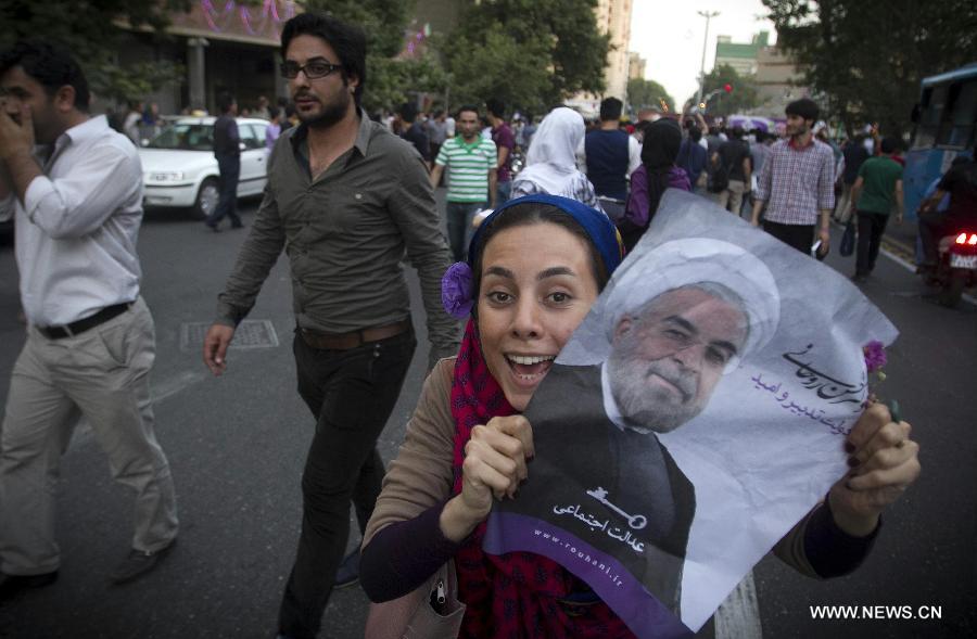 A woman shows a poster of Iran's former nuclear negotiator Hassan Rouhani to celebrate his victory at the presidential election on a street in Tehran, Iran, June 15, 2013. Hassan Rouhani defeated his rival conservative candidates in Iran's 2013 presidential election Saturday by gaining 18,613,329 votes out of counted votes of 36,704,156, accounting for 50.7 percent of all the votes, with a turnout rate of 72.2 percent. [Ahmad Halabisaz/Xinhua]