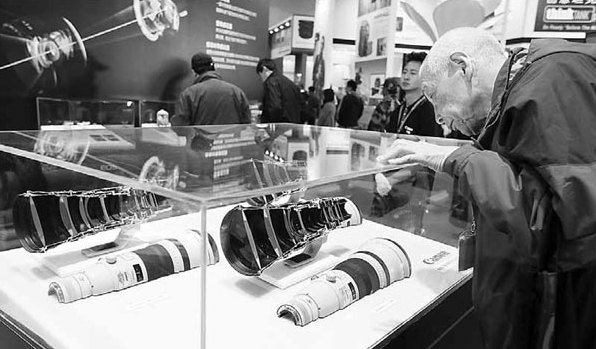A Beijing resident examining Canon telephoto lenses at the 16th China International Photograph and Electrical Imaging Machinery and Technology Fair in Beijing in April. [China Daily]