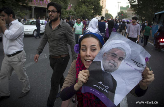 A woman shows a poster of Iran's former nuclear negotiator Hassan Rouhani to celebrate his victory at the presidential election on a street in Tehran, Iran, June 15, 2013. [Xinhua photo]