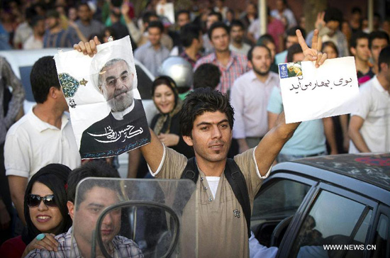 A man raises a poster of Iran's former nuclear negotiator Hassan Rouhani to celebrate his victory at the presidential election on a street in Tehran, Iran, June 15, 2013. [Ahmad Halabisaz/Xinhua]