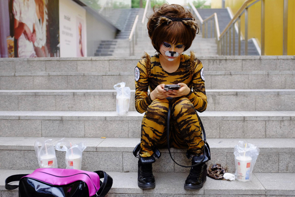 A volunteer wearing an animal costume checks her mobile phone as she waits to perform in an event promoting a love for dogs, in Beijing's Sanlitun area, on June 20, 2013.[Photo/China Daily via Agencies]