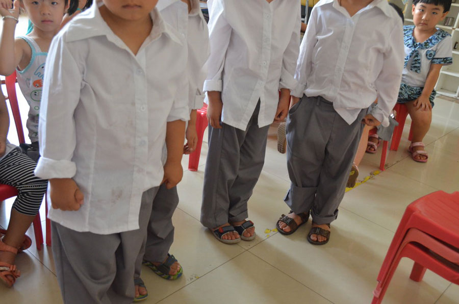 More than 80 kindergarten pupils were ordered to wear long-sleeved shirts whilst awaiting the arrival of local leaders, despite high temperatures on Monday.