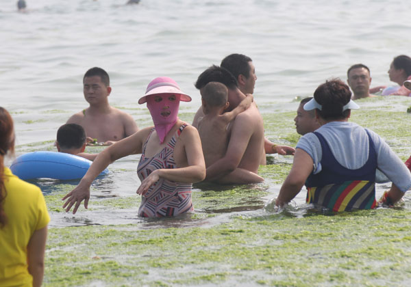 A woman protects herself with a face-kini and hat while playing in the water in Qingdao, a coastal city in Shandong province, on July 3, 2013. [Photo by Huang Xianjie/Asianewsphoto] 