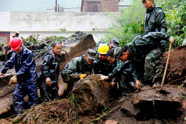 Rescuers examine a rock before they move it to rescue people buried underneath after a landslide in a village in Zhaotong, Yunnan province, on Friday. At least five people, including two children, were killed and four others injured in the accident. [Photo by Zhang Guangyu/For China Daily]