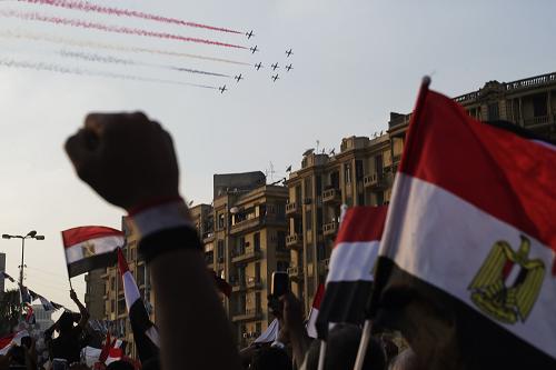 Egyptian people cheer and wave national flags as airplanes fly past the landmark Tahrir Square, trailing smoke in the colours of the national flag on July 4, 2013 in Cairo. [Xinhua/AFP] 