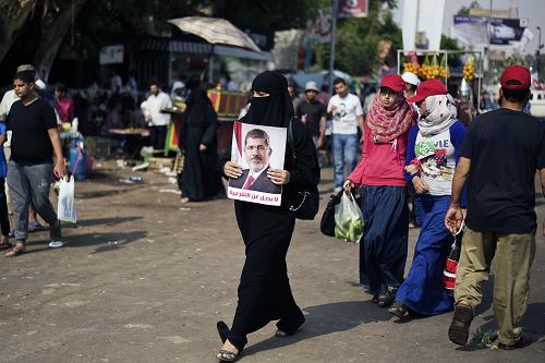 An Egyptian woman walks holding a portrait of ousted president Mohammed Morsi as thousands of his supporters gather in front of Cairo's Rabaa al-Adawiya mosque on July 9, 2013.[Xinhua/AFP]