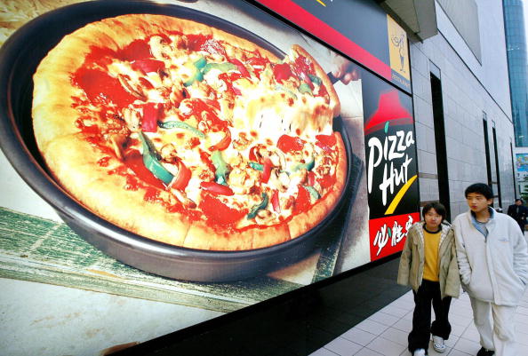 Two teenagers walk past a Pizzahut billboard in Shanghai. [File photo]