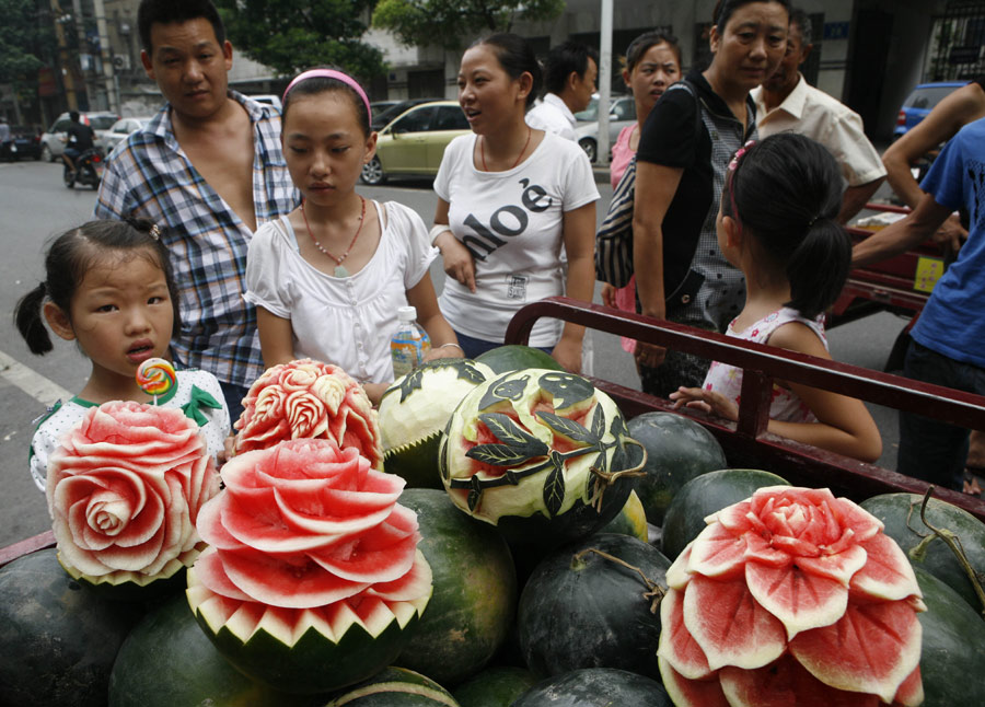 Customers are attracted by artistic watermelons in Xiangyang, Hubei province, on Monday, July 23, 2013. Zhang Yunxiao, a 30-year-old fruit dealer, carves vivid flowers like peonies and roses as well as other patterns on the melons. The price for each melon is 20 yuan ($3.26) to 50 yuan. [Photo / China Daily]