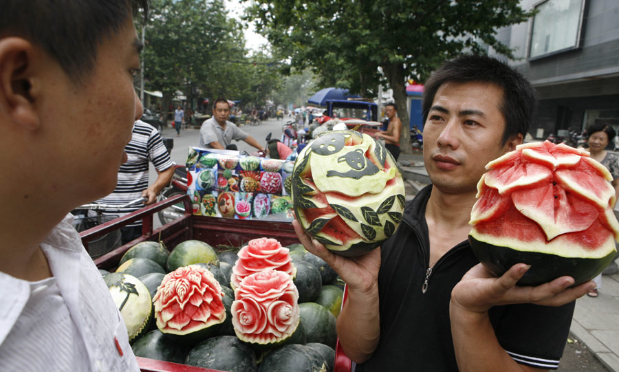 Zhang Yunxiao, a 30-year-old fruit dealer, tries to sell artistic watermelons to a customer in Xiangyang, Hubei province, on Monday, July 23, 2013. Zhang carves vivid flowers like peonies and roses as well as other patterns on the melons. The price for each melon is 20 yuan ($3.26) to 50 yuan. [Photo / China Daily]