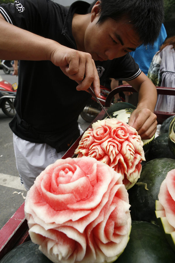 Zhang Yunxiao, a 30-year-old fruit dealer, tries to sell artistic watermelons to a customer in Xiangyang, Hubei province, on Monday, July 23, 2013. Zhang carves vivid flowers like peonies and roses as well as other patterns on the melons. The price for each melon is 20 yuan ($3.26) to 50 yuan. [Photo / China Daily]