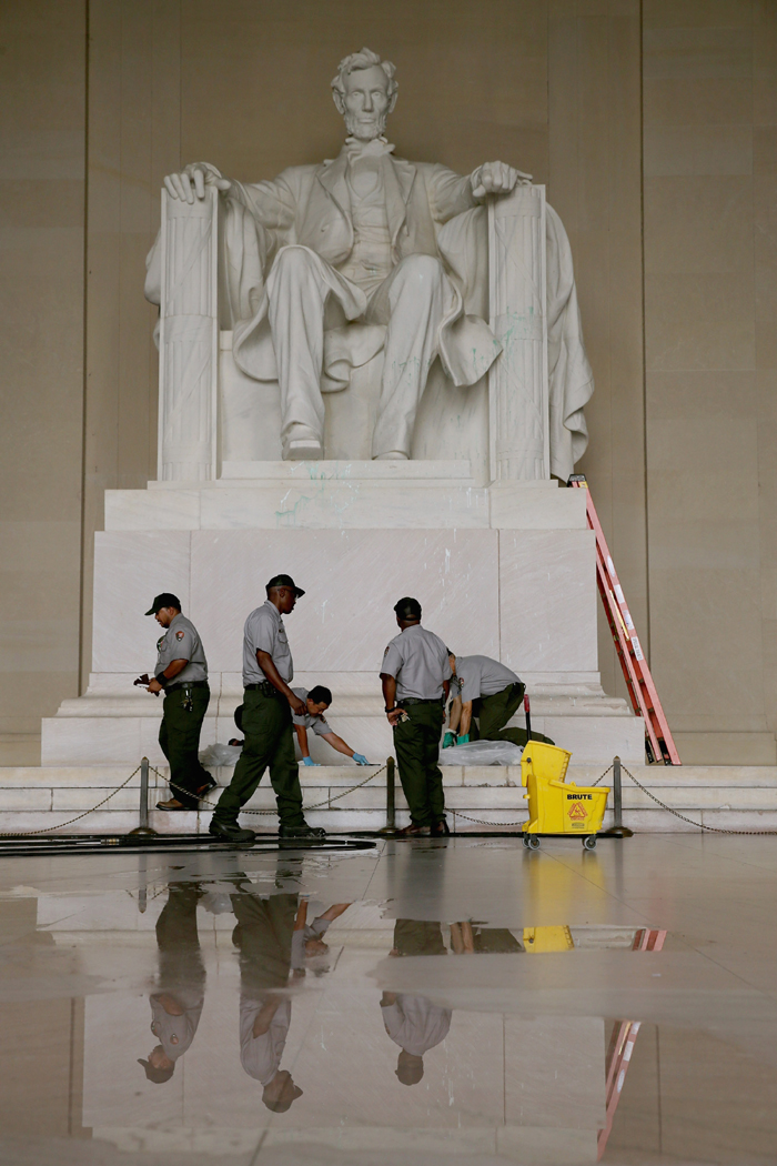 U.S. National Park Service employees use a variety of tools, including razor blades, plastic paint scrapers, sponges, solvents and a pressure washer, to clean the Lincoln Memorial after it was vandalized with a splatter of green paint July 26, 2013 in Washington, DC.