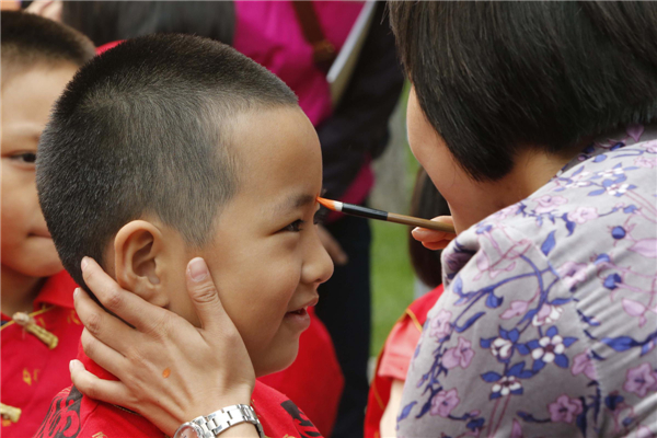 A boy is given a red dot on his forehead during a memorial ceremony to commemorate the 2,564th birthday anniversary of Confucius in Beijing, Sept 28, 2013. [Photo/Xinhua]