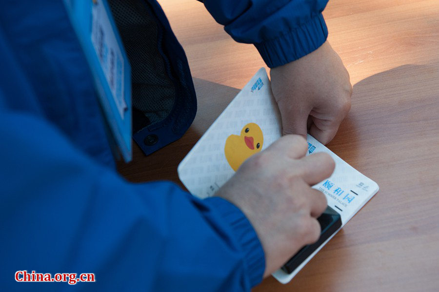 A staff member of Beijing Design Week, the organization committee for the display of Rubber Duck in Beijing, prints a souvenir stamp on a tourist's Rubber Duck Passport at the Summer Palace in Beijing on Sunday. [Photo / Chen Boyuan / China.org.cn]
