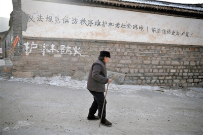 2012年12月31日，河北省阜平县，一村民走过写有关于信访政策的标语墙。[新京报 侯少卿 摄]