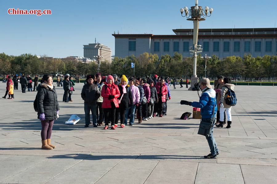 Tourists in Tian'anmen Square defy coldness in Beijing and pose for photos before the national flag stand on Wednesday. A strong cold snap that swept north China on Wednesday has brought down Beijing's temperature to below freezing point, sending the city into the depth of winter. The strong wind has completely dispersed the smog that used to hover above the Chinese capital. [Photo by Chen Boyuan / China.org.cn]