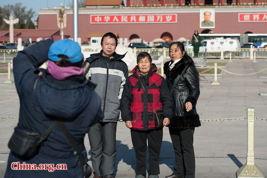 Tourists in Tian'anmen Square defy coldness in Beijing and pose for photos before the national flag stand on Wednesday. A strong cold snap that swept north China on Wednesday has brought down Beijing's temperature to below freezing point, sending the city into the depth of winter. The strong wind has completely dispersed the smog that used to hover above the Chinese capital. [Photo by Chen Boyuan / China.org.cn]