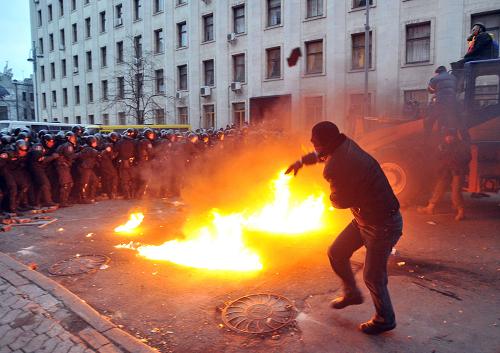 A protester throws stones towards riot police during the storming of the Viktor Yanukovych Presidential office in Kiev during a mass rally of the opposition in Kiev on December 1, 2013. The crowd chanted 'Revolution!' and 'Down with the Gang' as it took control of Kiev's iconic Independence Square and steered a bulldozer within striking distance of police barricades protecting the nearby presidential adminstration office.[Xinhua photo] 