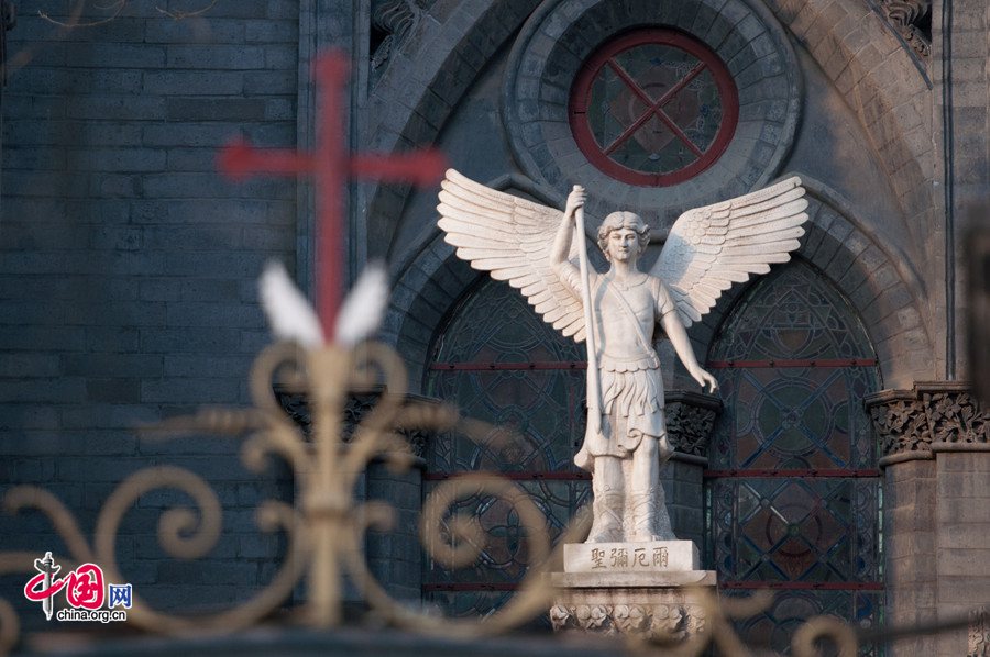 The statue of Michael the Angel, the guardian angel of St. Michael&apos;s Church (also known as French Legation Church and Dongjiaominxiang Church) stands in Beijing&apos;s winter coldness, facing an iron cross on top of the church gate on Dec. 25, Christmas Day. [Photo by Chen Boyuan / China.org.cn]