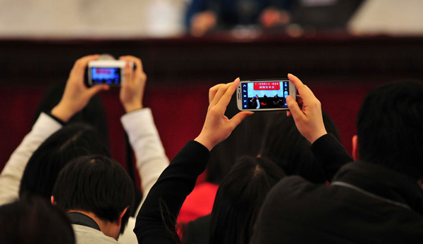 Two reporters take pictures with smart phones on the morning of March 4, 2014. The press conference for the second session of the 12th National People's Congress was held in the Great Hall of the People on that day. [Chinanews/Jin Shuo]