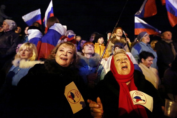 Two women hold flags reading 'Crimea is with Russia' as people wait for the announcement of preliminary results of today's referendum on Lenin Square in the Crimean capital of Simferopol March 16, 2014. [Photo/China Daily]