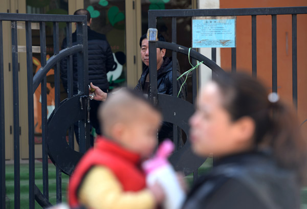 A mother holds her son at the gate of a private kindergarten, Hongji Xincheng, in Xi'an, Shaanxi province, on Thursday. Investigators said school officials administered prescription antiviral drugs to children. The number of children who were given the medicine was raised to 1,455.[Photo/Xinhua]