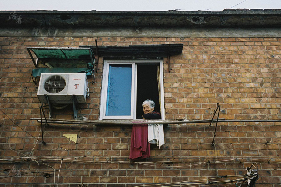 A woman looks out of the window of her home, which was built in the 1960s.[Photo/qq.com] 