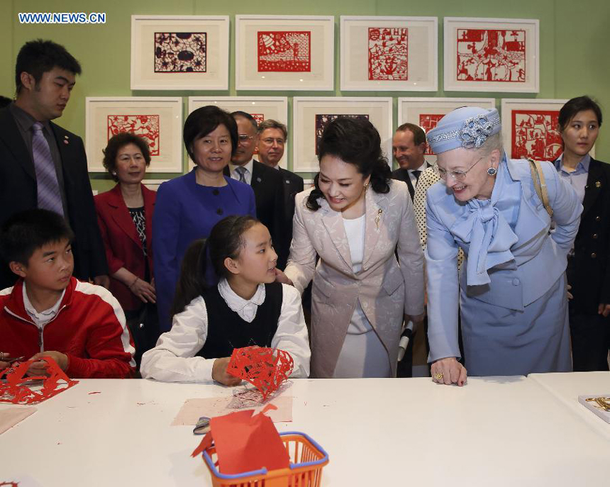 Chinese President Xi Jinping&apos;s wife, Peng Liyuan (2nd R, front) and Danish Queen Margrethe II (1st R, front) talk with a girl who is making paper-cut figures in Beijing, capital of China, April 25, 2014. Queen of Denmark Margrethe II visited an exhibition on Hans Christian Andersen&apos;s fairy tales accompanied by Peng here on Friday.