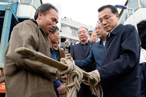 Premier Li Keqiang examines the pole of a bangbang, a traditional porter who helps residents carry bags, at Wanzhou port in Chongqing on Sunday. [China News Service] 