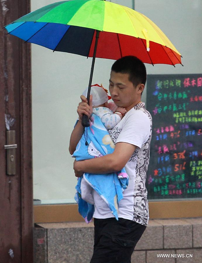 A man holding a baby walks under an umbrella in east China's Shanghai Municipality, June 26, 2014. Parts of Shanghai received torrential rain Thursday. [Photo/Xinhua]