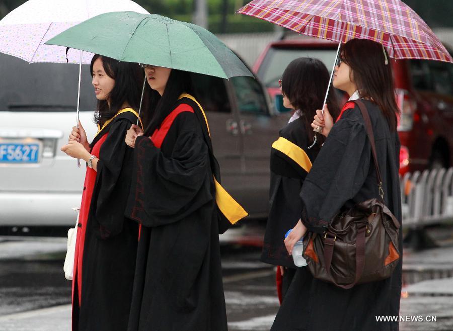 College students in academic dresses walk under umbrellas in east China's Shanghai Municipality, June 26, 2014. Parts of Shanghai received torrential rain Thursday. [Photo/Xinhua]