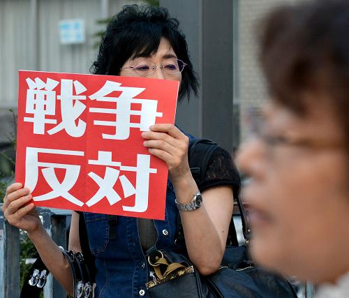 A woman holds a placard 'opposing the war' during an anti Abe government rally in front of the prime minister's official residence in Tokyo on July 2, 2014. Shinzo Abe proclaimed Japan's powerful military had the right to go into battle in defence of allies, so-called 'collective self-defence', in a highly contentious change in the nation's pacifist stance. [Xinhua photo]