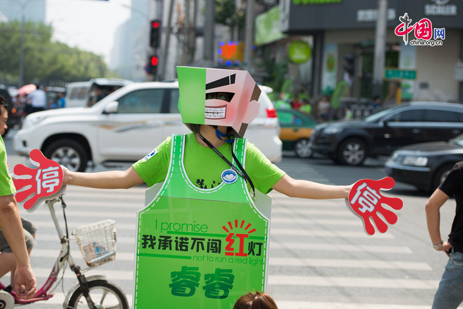 A volunteer traffic warden dressed like a robot, or &apos;transformer,&apos; as he prefers, shows his gagets in directing pedestrians at crossroads with traffic lights. The local government of east Beijing&apos;s Chaoyang District initiates a campaign entitled &apos;I promise not to run a red light&apos; on Tuesday, July 8, 2014, in a bid to eliminate jaywalking in this flourishing part of the Chinese capital. [Photo by Chen Boyuan / China.org.cn]