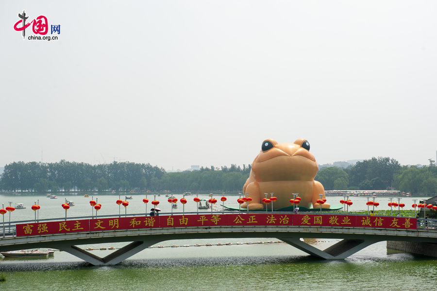 A giant, air-filled toad is seem at the lake of the Yuyuantan Park in downtown Beijing on Saturday, July 19, 2014. The 22-meter tall toad, called &apos;Toad of Rejuvenation&apos; or simply &apos;Golden Toad,&apos; is meant to represent the traditional Chinese culture as it brings blessings and fortune. The appearance of the Golden Toad can hardly make people refrain from comparing it with the Giant Rubber Duck, an artifact made by Dutch artist Florentijn Hofman, famous worldwide. [Photo by Chen Boyuan / China.org.cn]