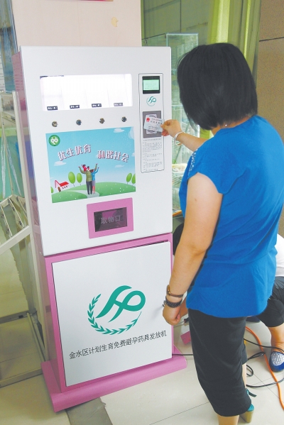 A staff member from Jinshui district health and family planning department, Zhengzhou, Henan province, shows how to use the new condom distribution machine on July 23, 2014. [Photo: dahe.cn]