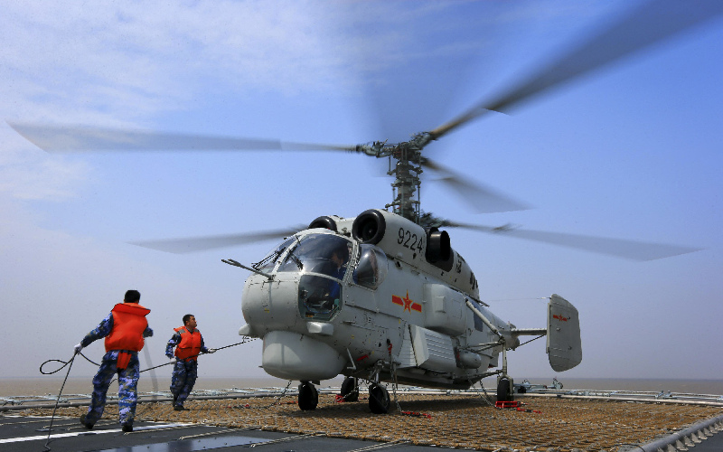 Logistics personnel maintain a helicopter on board a missile destroyer.