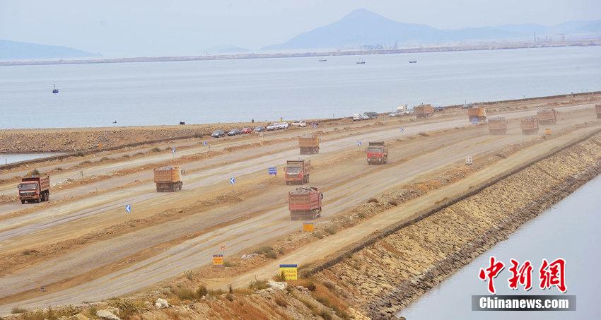 Photo taken on September 14, 2014, shows trucks running on the Jinzhouwan International Airport construction site to remove soil from a mountain nearby to the offshore area.
