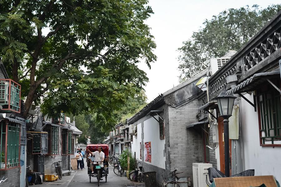 Cao Junlai points at a traditional Beijing house and introduces the hutong to tourists on his rickshaw in Beijing, Sept 12, 2014. [Photo/Xinhua]