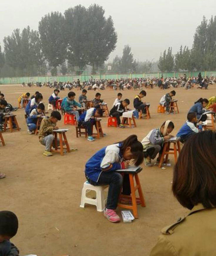 Hebei province has released an alarm on the thick smoke in Handan County. Some students in Handan squat on the outdoor playground to take their midterm exam on October 9, 2014. [Photo: sina.com.cn]