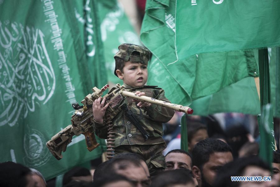 A Palestinian boy wears the headband of Hamas armed wing as he sits on the shoulder of his father during a rally ahead of the 27th founding anniversary of Hamas, in Jabaliya refugee camp in the northern Gaza Strip, on Dec. 12, 2014.