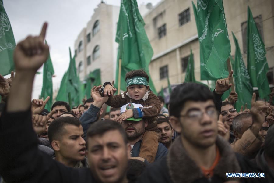 A Palestinian boy wears the headband of Hamas armed wing as he sits on the shoulder of his father during a rally ahead of the 27th founding anniversary of Hamas, in Jabaliya refugee camp in the northern Gaza Strip, on Dec. 12, 2014.