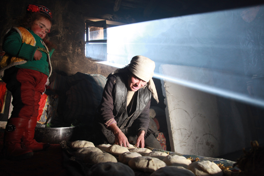 Gulaxiami looks on as her aunt prepares to make naan, the staple wheat bread of the Uygur autonomous region. [Photo by Wang Lie/chinadaily.com.cn]
