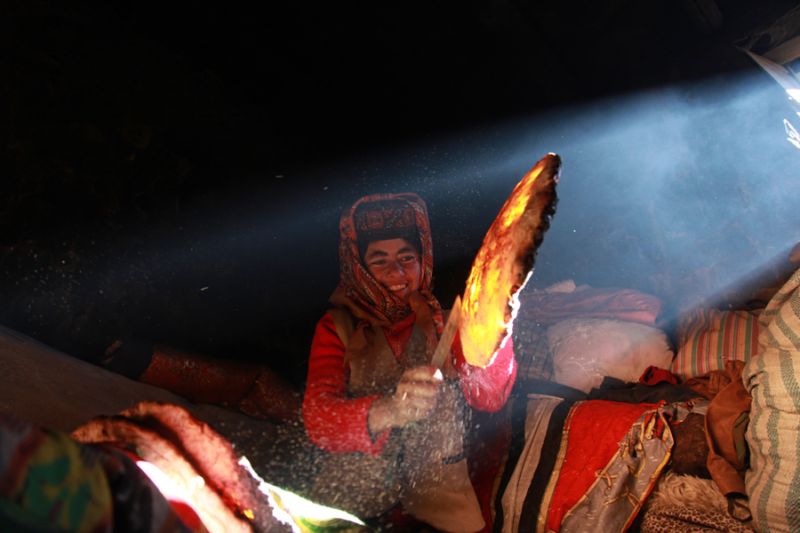 A woman takes a naan out from a hand-made clay pit. [Photo by Wang Lie/chinadaily.com.cn]