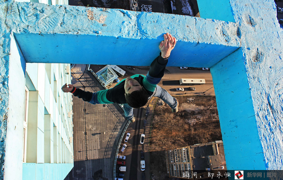 A Russian adventurer enthusiast hangs off the edge of a building several hundred meters above the ground with one hand. [Photo/Xinhuanet]