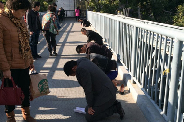 People dressed in formal suits kneel down on a pedestrian bridge in Xiamen, East China's Fujian province, on Sunday. [Photo/Sina weibo] 