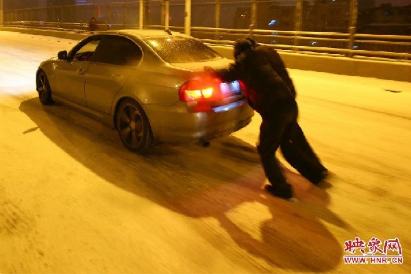 Two men push a car in snow in Zhengzhou, capital of Central China's Henan province. [Photo.hnr.cn]