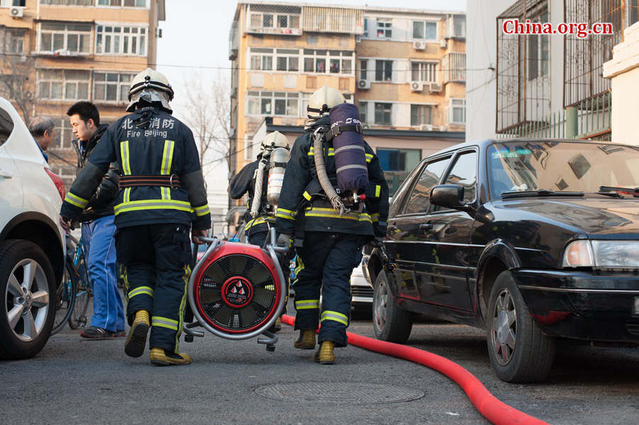 Firefighters prepare professional tools in trying to put out a fire in a residential area in downtown Beijing on Thursday, March 5, the traditional Chinese Lantern Festival. The blazing building is located between Linglong Rd. and Qixiancun Rd. in Haidian District, is used as a warehouse of Gehua, Beijing&apos;s local cable TV service provider. The burning rubber from the cable wire gives out a strong black smoke. [Photo by Chen Boyuan / China.org.cn]