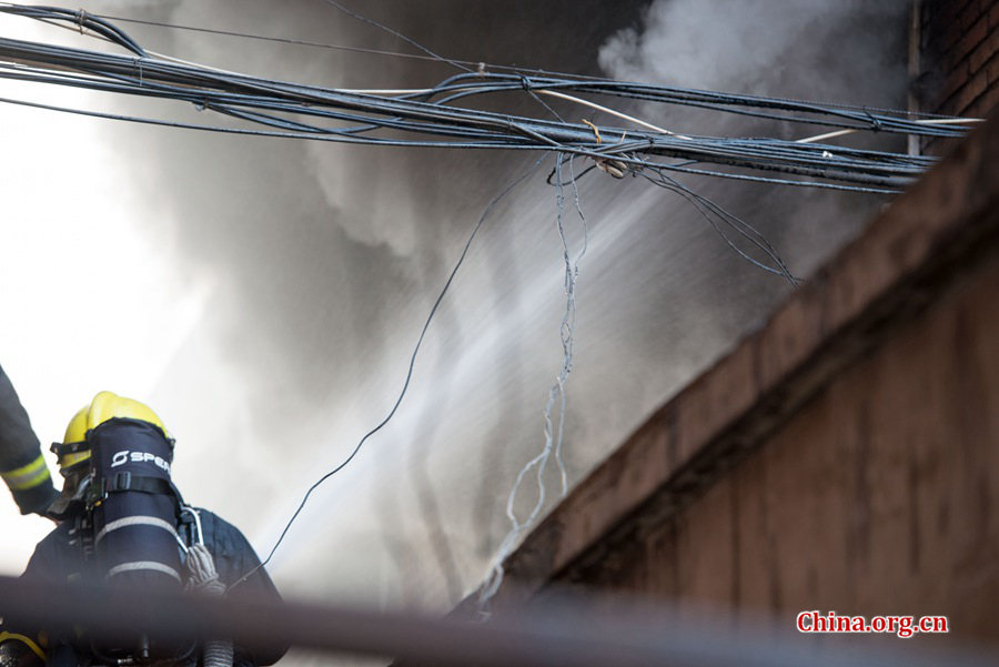 Firefighters pump water into a blazing building in a residential area in downtown Beijing on Thursday, March 5, the traditional Chinese Lantern Festival. The building located between Linglong Rd. and Qixiancun Rd. in Haidian District, is used as a warehouse of Gehua, Beijing&apos;s local cable TV service provider. The burning rubber from the cable wire gives out a strong black smoke. [Photo by Chen Boyuan / China.org.cn]