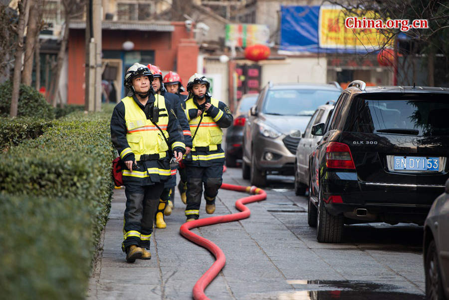 Firefighters prepare professional tools in trying to put out a fire in a residential area in downtown Beijing on Thursday, March 5, the traditional Chinese Lantern Festival. The blazing building is located between Linglong Rd. and Qixiancun Rd. in Haidian District, is used as a warehouse of Gehua, Beijing&apos;s local cable TV service provider. The burning rubber from the cable wire gives out a strong black smoke. [Photo by Chen Boyuan / China.org.cn]